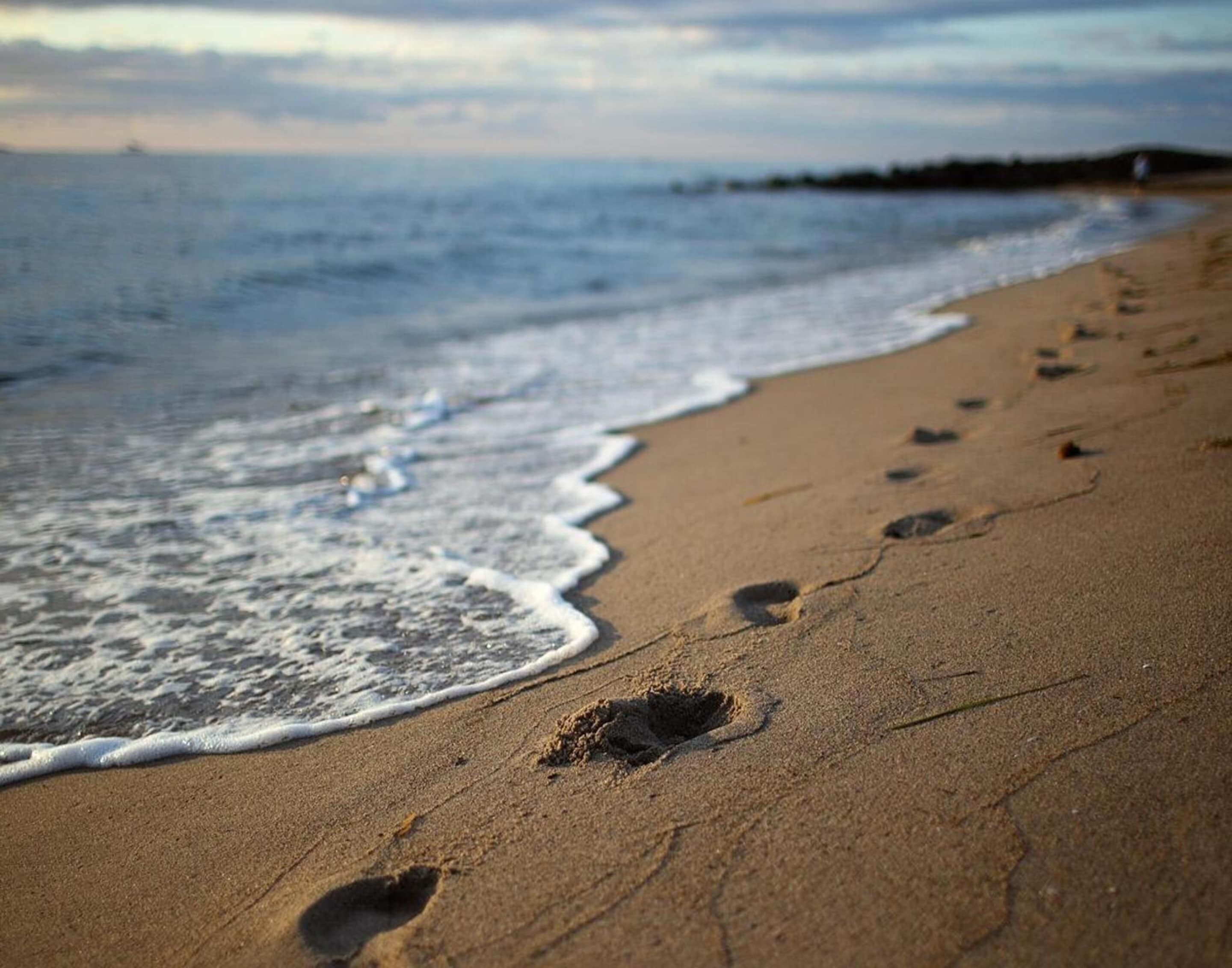 Une plage de sable où l’on peut voir des empreintes de pas qui mènent jusqu’au bord de l’eau.