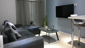 Ein modernes Wohnzimmer mit grauem Sofa, einem runden Couchtisch und einem an der Wand montierten Fernseher.