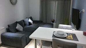 Ein modernes Wohnzimmer mit grauem Sofa, einem weißen Esstisch und einem Weinglas.