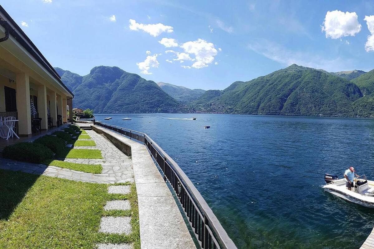 A lakeside view with a boat docked, a stone pathway, and a building with a balcony.