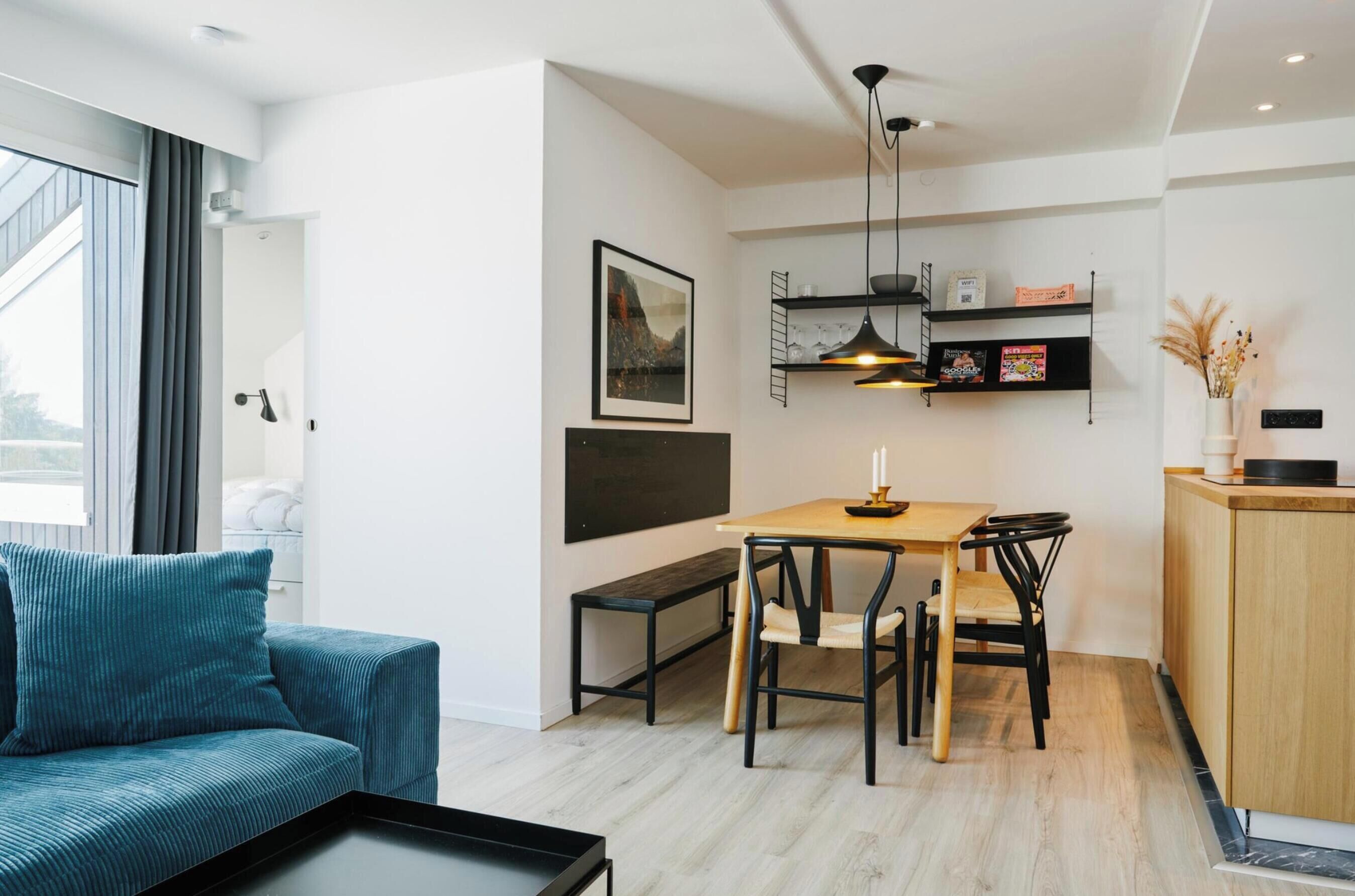 A modern interior with a sofa, dining table, chairs, a bench, a kitchen area with shelves, and a hanging light fixture.