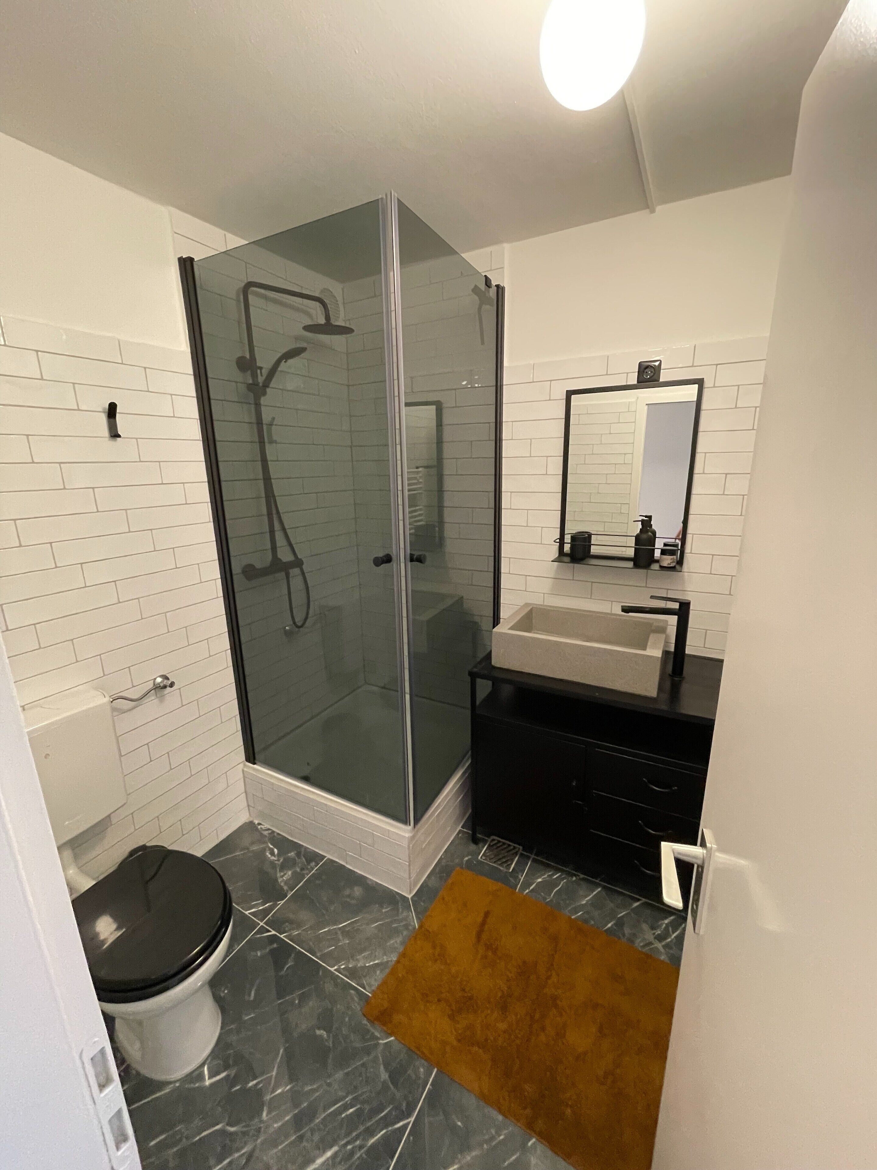 Un baño moderno con ducha envuelta en cristal, inodoro, lavamanos y espejo.