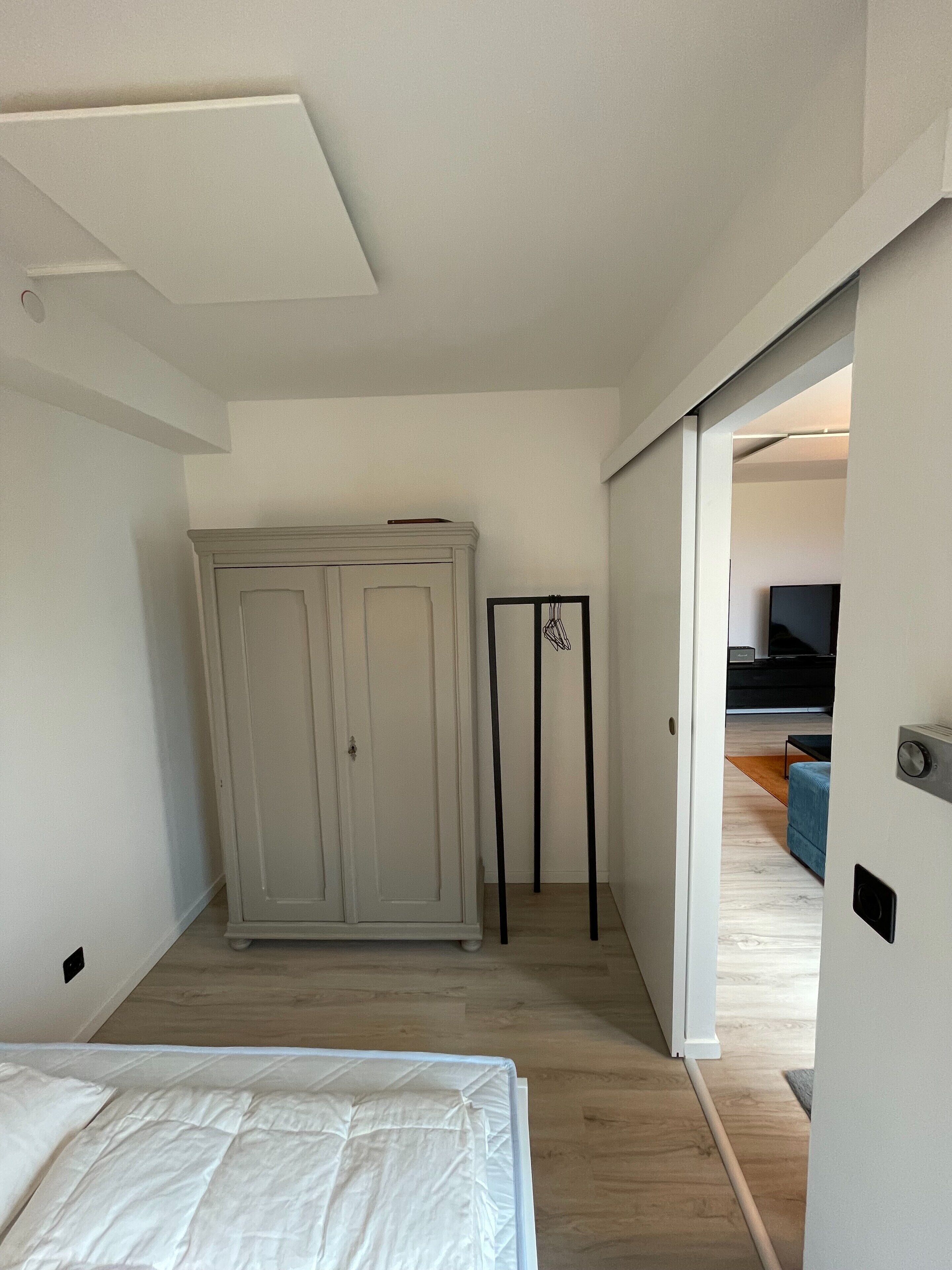 A bedroom with a bed, a wardrobe, and a door leading to another room.
