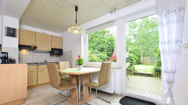 A kitchen with a dining table, chairs, a microwave, and a view of a garden through a window. - Garden-view Apartment in Heringhausen Lake City Centre (Diemelsee)