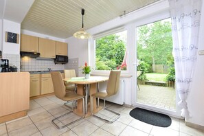 A kitchen with a dining table, chairs, a microwave, and a view of a garden through a window. - Garden-view Apartment in Heringhausen Lake City Centre (Diemelsee)