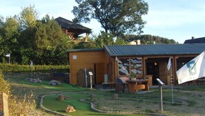 A wooden cabin with a small patio, a flag, and a golf course in the background. - Garden-view Apartment in Heringhausen Lake City Centre (Diemelsee)