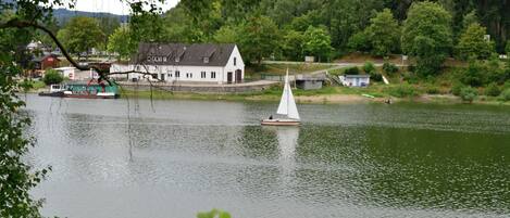 Un lago tranquilo con un velero, una casa blanca y un muelle con una grúa.