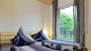 A bed with patterned bedding and pillows, a wooden headboard, and a window with curtains. - Garden-view Apartment in Heringhausen Lake City Centre (Diemelsee)