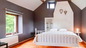 A bedroom with a sloped ceiling, a bed with white bedding, a window with a view of greenery, and a small shelf unit. - Beautiful Gite in Jalhay 5 Minutes From the Hautes Fagnes (Jalhay)