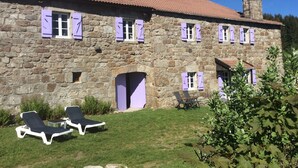 Un edificio de piedra con varias ventanas y una chimenea. Hay dos sillones en primer plano.