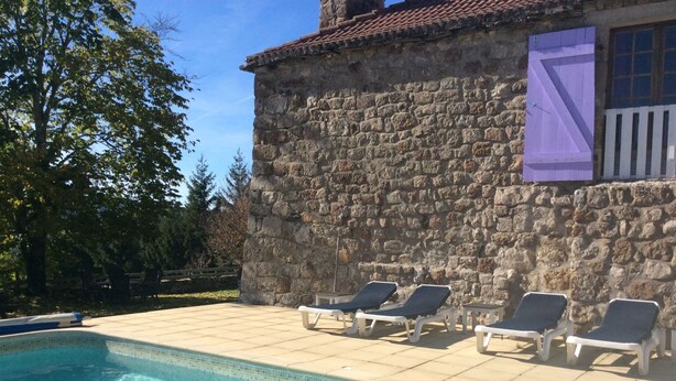 Edificio de piedra con zona de piscina con azulejos, incluyendo sillas de descanso y una piscina pequeña.