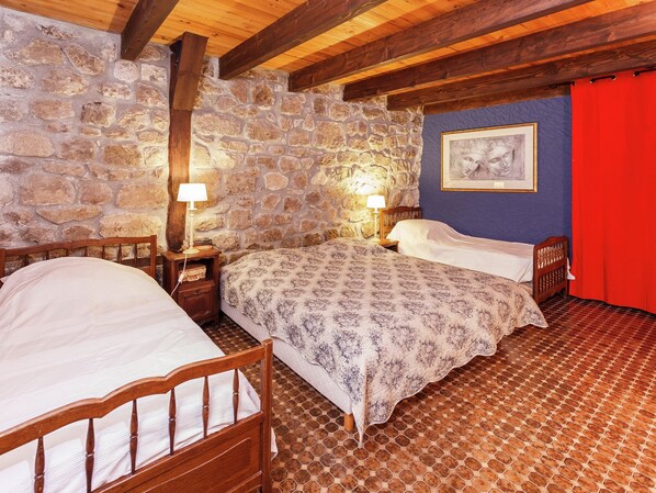 A bedroom with two beds, stone walls, wooden beams, a tiled floor, and a red curtain.