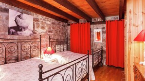 Un dormitorio con pared de piedra, cama con estructura metálica, cortinas rojas y suelo de madera.