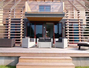 Une maison moderne avec une façade en bois, de grandes portes vitrées et un espace salon extérieur.