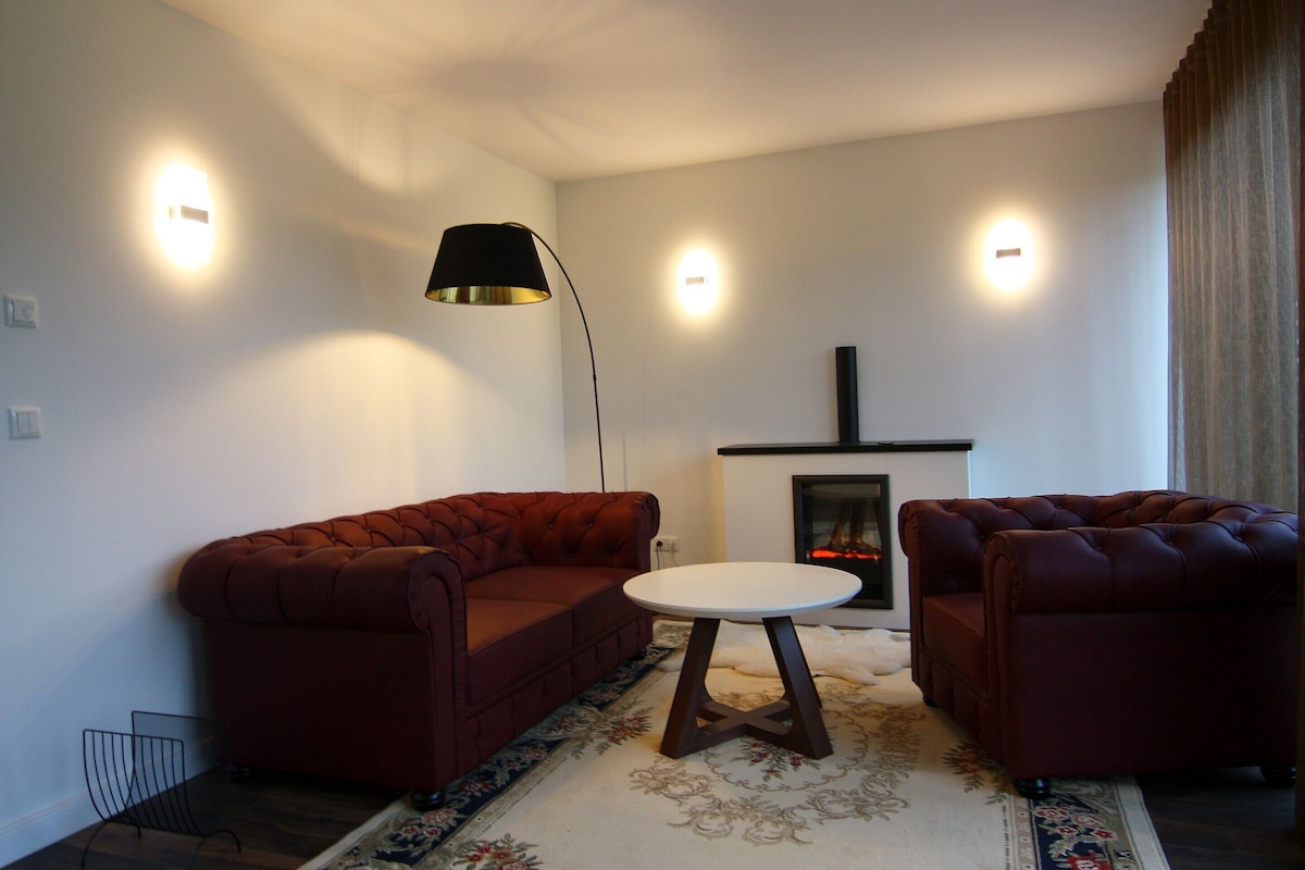 Ein Wohnzimmer mit einer Sofagarnitur, einem kleinen runden Tisch, einer Stehlampe und einem Kamin.
