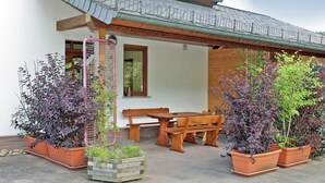 A covered patio with wooden furniture, potted plants, and a birdcage. - Beautiful and Cosy Apartment in a Wooded and Mostly Quite Rustic Ambience (Balesfeld)