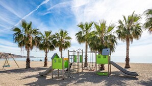 A beach playground with slides and climbing structures, palm trees, and a clear view of the sea. - Beautiful and Cosy Apartment in a Wooded and Mostly Quite Rustic Ambience (Balesfeld)