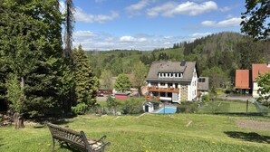 Une maison avec un grand jardin devant, un banc et une piscine.