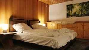Une chambre à coucher avec une tête de lit en bois, un lit recouvert de draps blancs, une table de chevet avec une lampe, une commode en bois et un tableau sur le mur représentant une forêt.