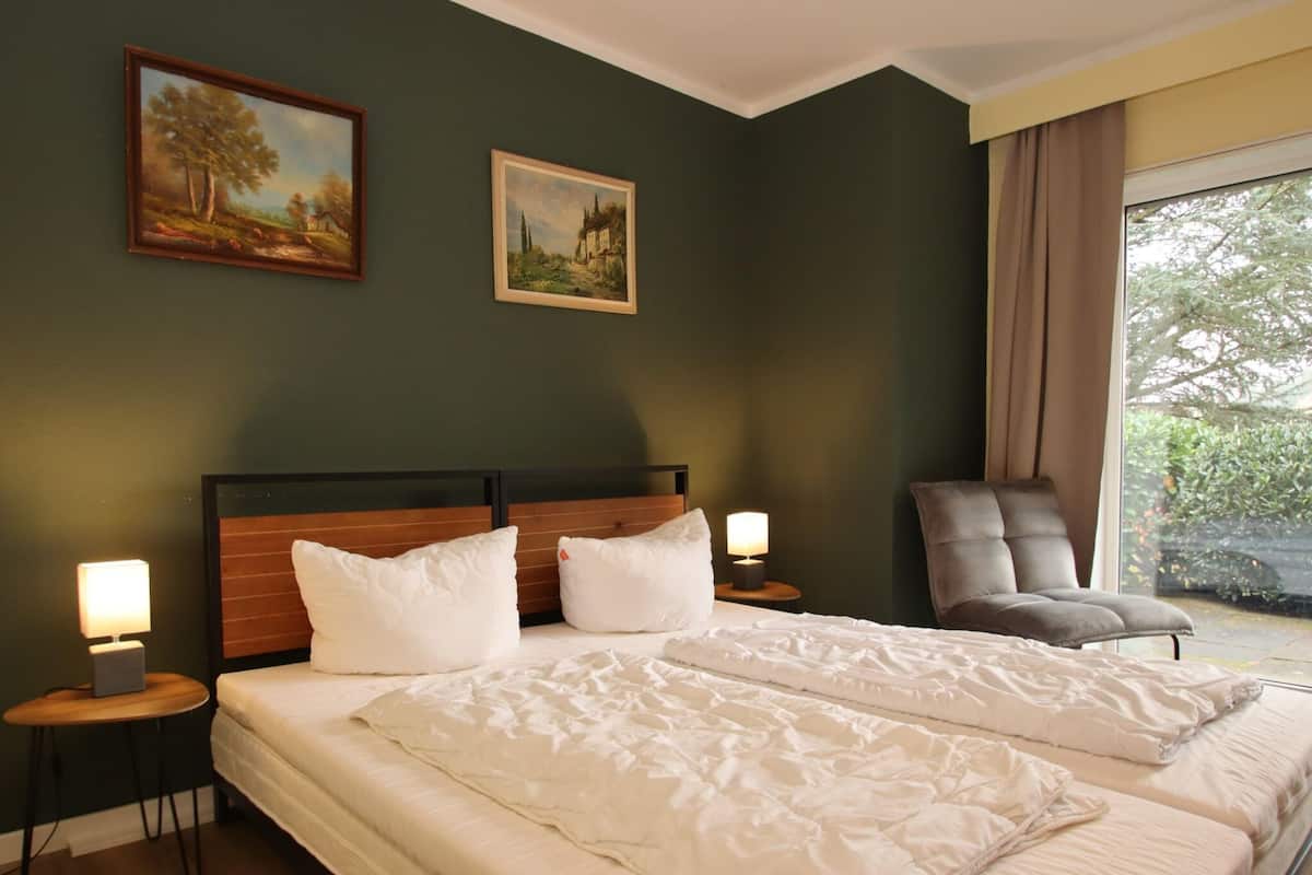 Une chambre d’hôtel avec deux lits, une tête de lit en bois, une chaise et deux tableaux accrochés au mur.