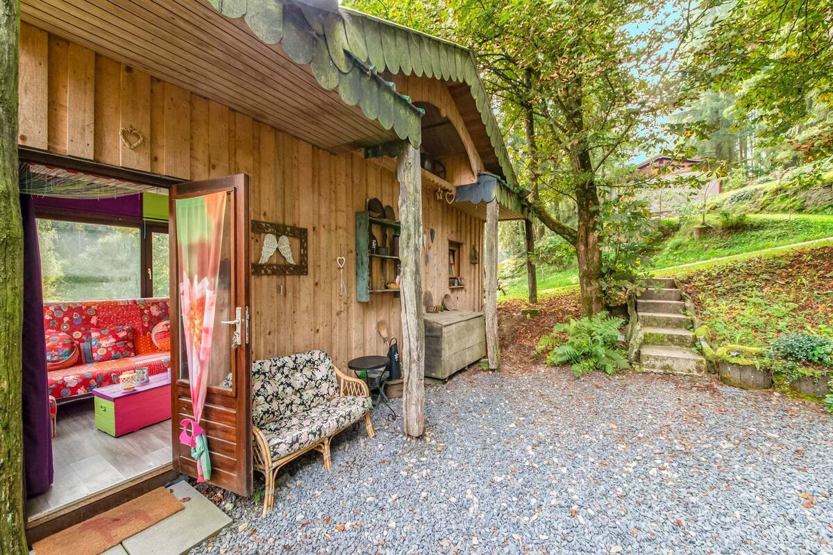 A wooden cabin with a porch, a seating area with cushions, and a gravel driveway.
