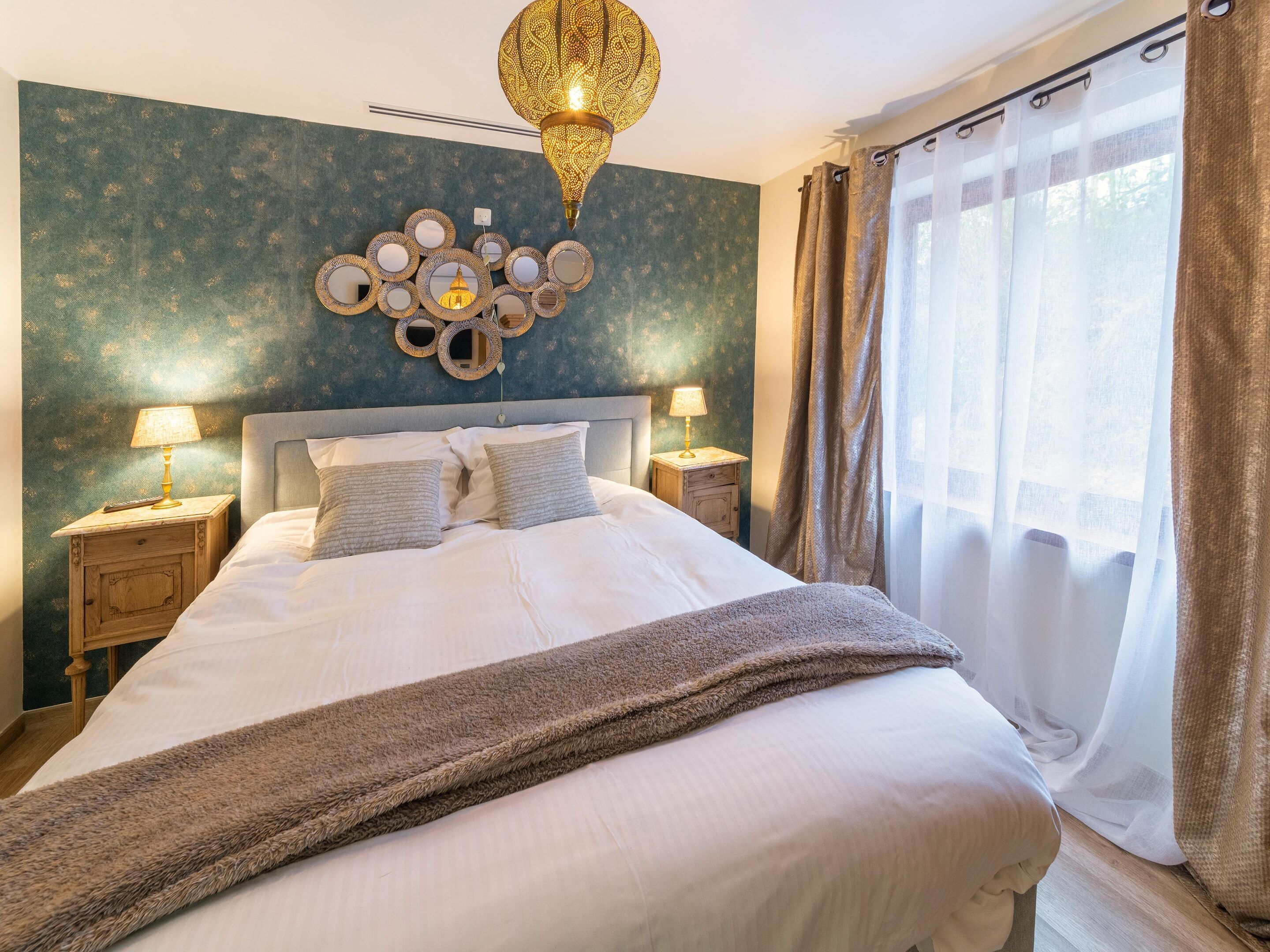 A neatly made bed with two pillows, a decorative wall piece above it, and a hanging light fixture.