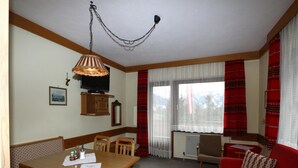 Ein Zimmer mit einem Holzesstisch, Stühlen, einem roten Sofa, einem Fernseher und einem Fenster mit roten Vorhängen.