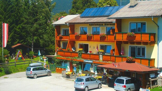 Ein Hotel mit mehreren Balkonen, einem Parkplatz und einer Bergkulisse.