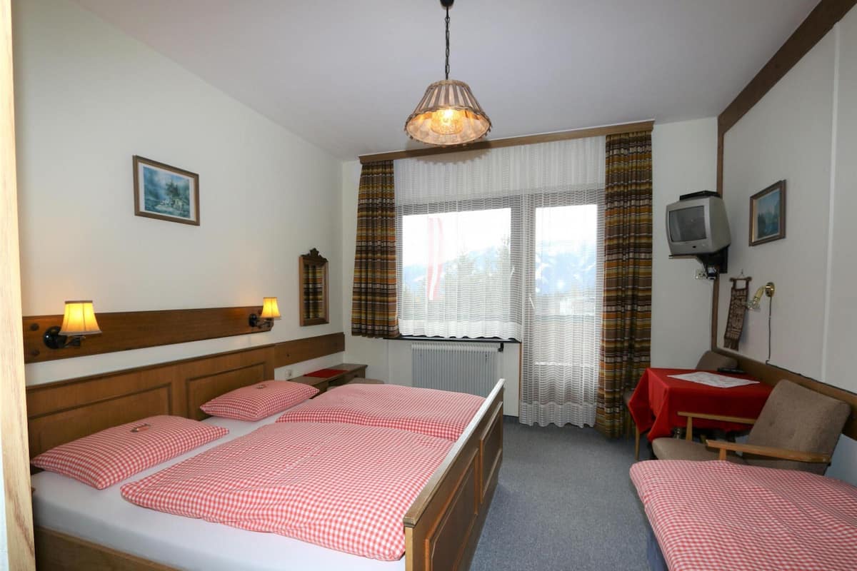 Hotellihuone, jossa on suuri sänky, kaksi yöpöytää, työpöytä tuolilla, televisio ja ikkuna, jossa on verhot.