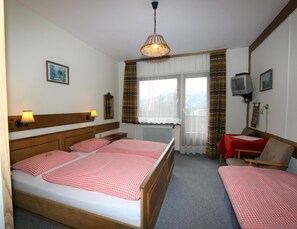 Ein Hotelzimmer mit einem großen Bett, zwei Nachttischen, einem Schreibtisch mit Stuhl, einem Fernseher und einem fenster mit Vorhängen.