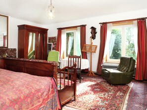 A traditional room with a bed, a green chair, a wooden music stand, and a radiator.