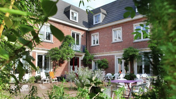 A courtyard with a patio area, outdoor seating, and a brick building with multiple windows and a balcony. - Comfortable Mansion in Doomkerke Near Forest (Ruiselede)