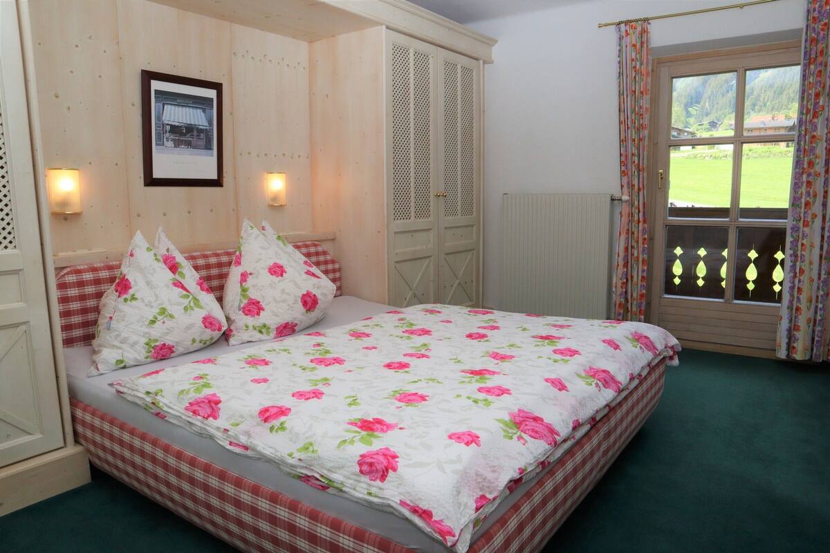Ein Schlafzimmer mit einem Bett, einem Holzschrank, einem Fenster mit Vorhängen und einem gerahmten Bild an der Wand.