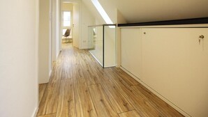 Un couloir étroit doté d’un plancher en bois, d’une cloison en verre et d’une porte donnant sur une autre pièce.