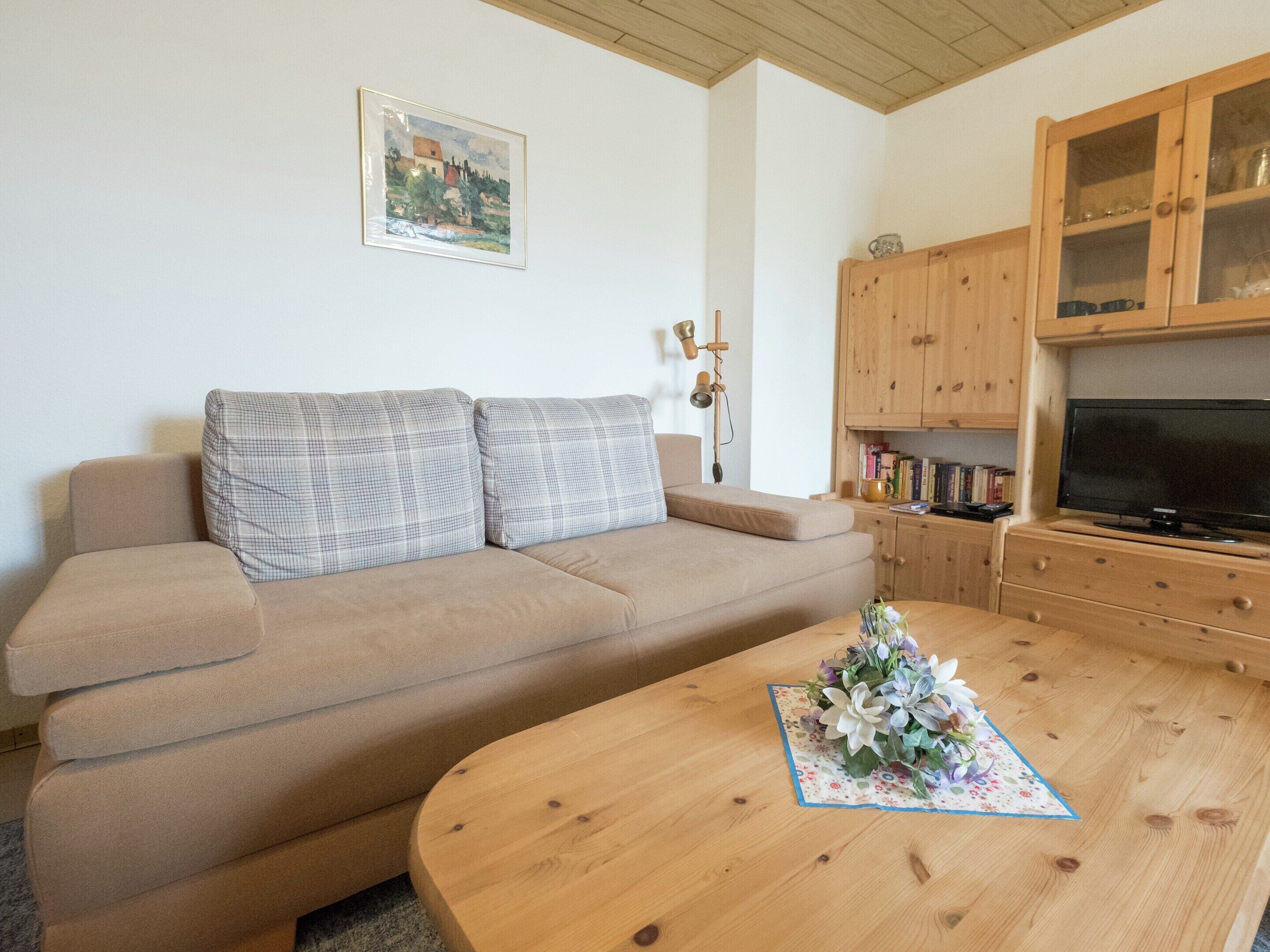 A living room with a beige sofa, a wooden coffee table with a floral centerpiece, a television, and wooden cabinets.