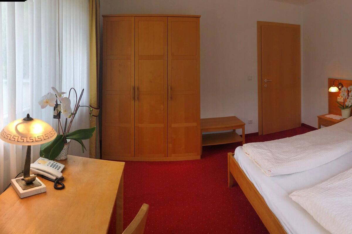 Ein Hotelzimmer mit Bett, Nachttischen, Schreibtisch mit Lampe, Kleiderschrank und einem kleinen Tisch.