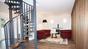 A modern living room with a spiral staircase, red sofas, a round coffee table, and a patterned rug. - Chalet, Wendorf (Kuhlen-Wendorf)