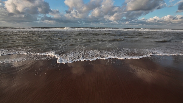 Een strand met golven, een zandstrand en een gedeeltelijk bewolkte lucht.