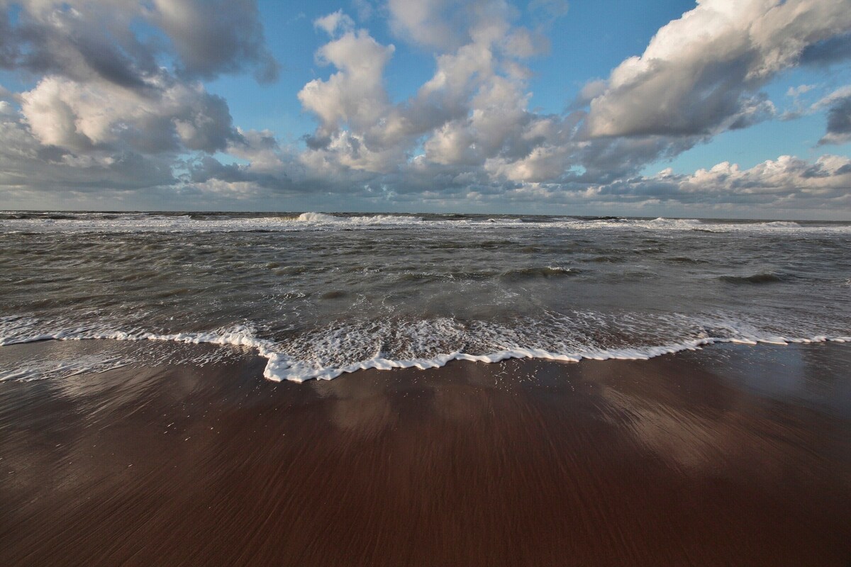 Una playa con olas, una orilla arenosa y cielo parcialmente nublado.