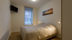 Een slaapkamer met een bed, een raam met zonwering, een aan de muur bevestigde televisie en een schilderij.