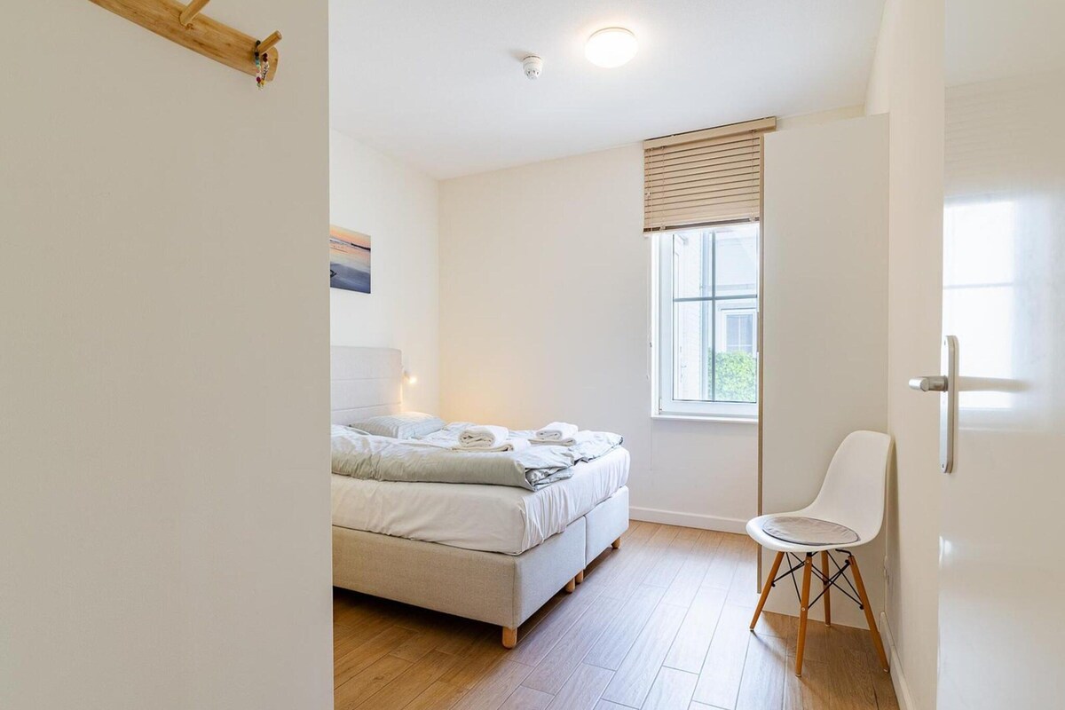 Un dormitorio con cama, una silla, un ventanal y una puerta.
