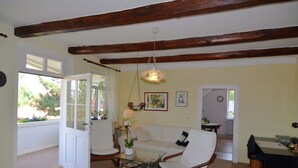 A living room with a white sofa, a glass coffee table, and a wooden ceiling beam. There is a door leading to another room and a window with curtains. - Modern Apartment in a Listed Villa With Beautiful View From Balcony (Quedlinburg)