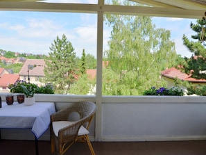 Ett takförsett utomhusområde med bord och stolar, med utsikt över ett bostadsområde med hus och träd.