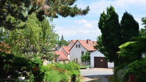 A cobblestone path leading to a white building with a red roof, surrounded by lush greenery and tall trees. - Modern Apartment in a Listed Villa With Beautiful View From Balcony (Quedlinburg)