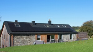 A modern house with a sloped roof, stone walls, and a large open patio area. - Modern Cottage in Vaux-sur-sure With Sauna (Vaux-sur-Sure)