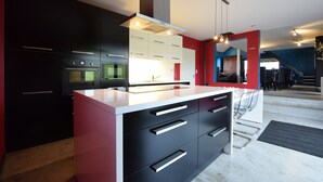 A modern kitchen with black and white cabinetry, stainless steel appliances, and a central island with drawers. - Modern Cottage in Vaux-sur-sure With Sauna (Vaux-sur-Sure)