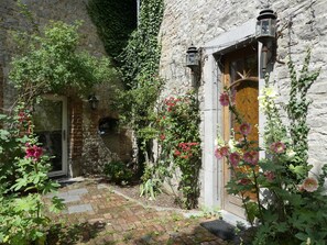 A stone building with a wooden door, a brick pathway, and various plants and flowers. - Holiday Home not far From the Small Town of Durbuy (Durbuy)