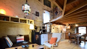 Un interior rústico con una mesa de comedor de madera, un sofá con almohadones a rayas, una mesa de centro y una zona de cocina con microondas y estufa.