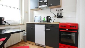 A compact kitchen with a microwave, oven, and a small refrigerator. There is a wooden countertop and a red chair. - Apartment in Malchow With Terrace (Malchow)