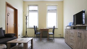 A compact living room with a sofa, a small table, two chairs, a TV on a stand, and a cabinet. - Apartment in Malchow With Terrace (Malchow)